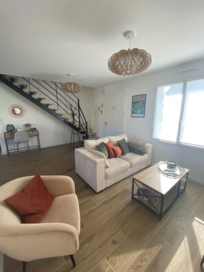 Una sala de estar con sofá, mesa de centro, escalera y un ventanal grande.