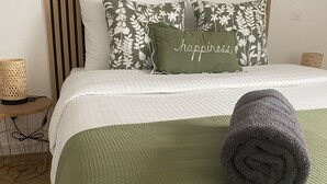 Cama bem arrumada com manta verde, toalha enrolada e almofadas estampadas.
