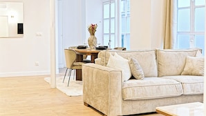 Ein modernes Wohnzimmer mit einem beigefarbenen Sofa, einem Esstisch mit Stühlen und einer Vase mit Blumen.