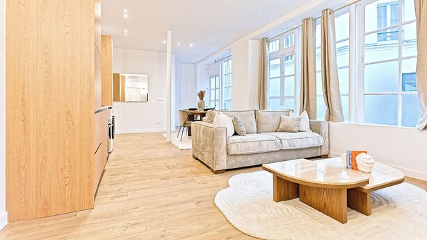 Ein modernes Wohnzimmer mit Sofa, Couchtisch und großen Fenstern.