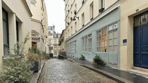 Eine enge Kopfsteinpflasterstraße, gesäumt von Gebäuden mit großen Fenstern und einer blauen Tür auf der rechten Seite.