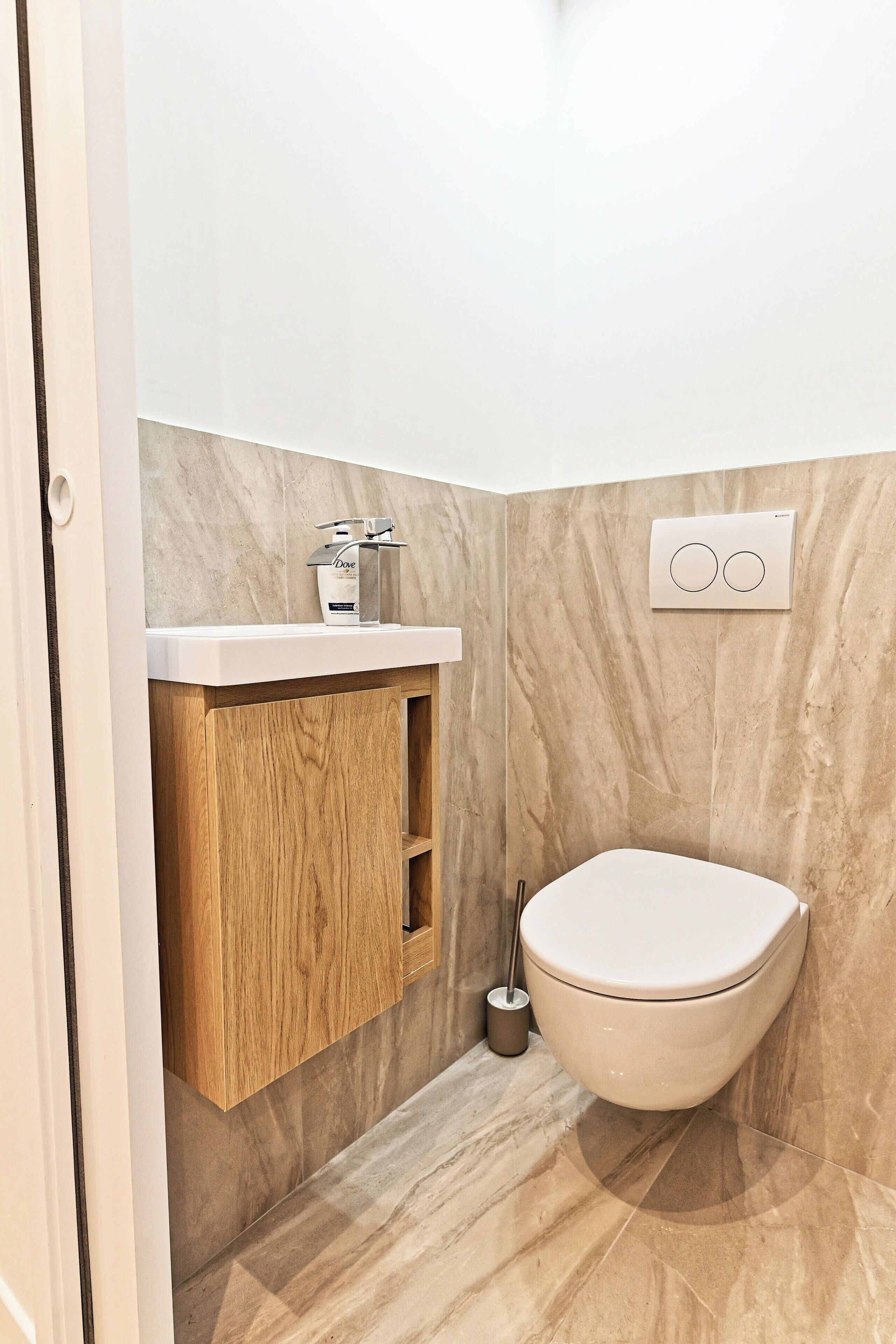 Une salle de bain moderne avec un mur en marbre, un meuble-lavabo en bois, des toilettes et un interrupteur fixé au mur.