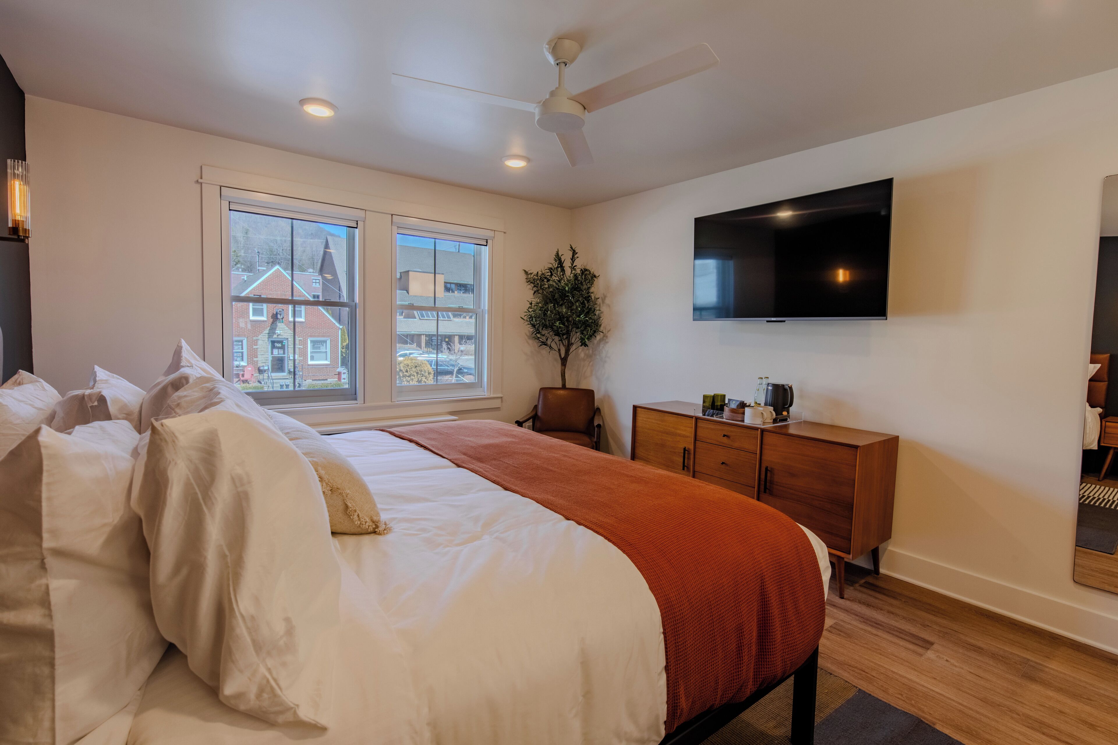 A hotel room with a large bed, a desk, a chair, a television, and a window with a view of buildings.