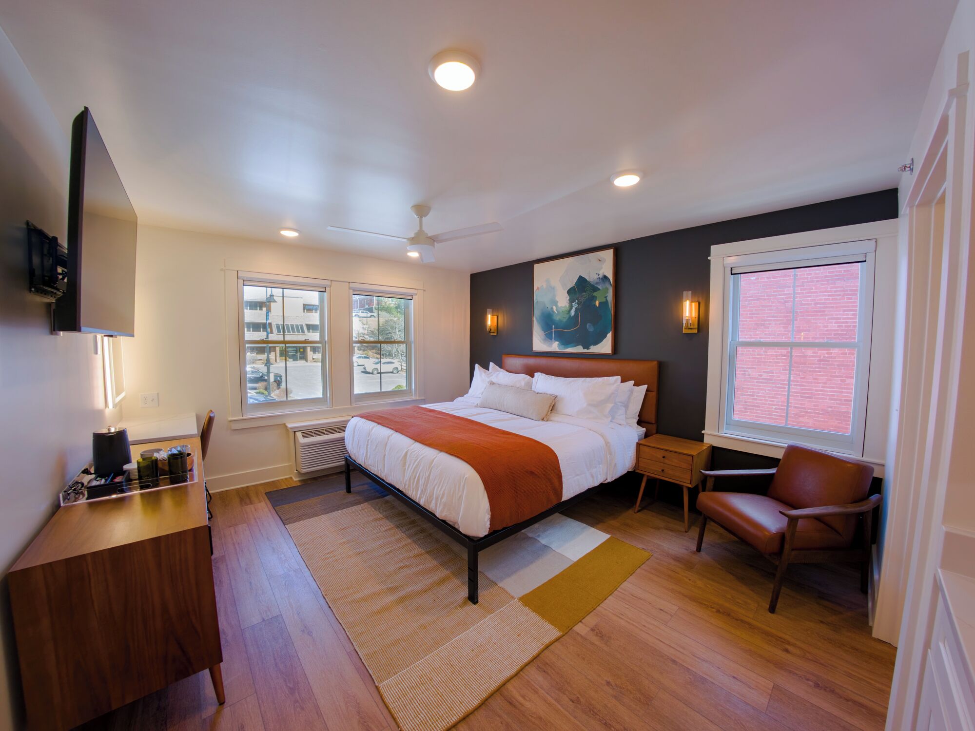 A modern bedroom with a large bed, a desk, a chair, and a window with a view of the street.