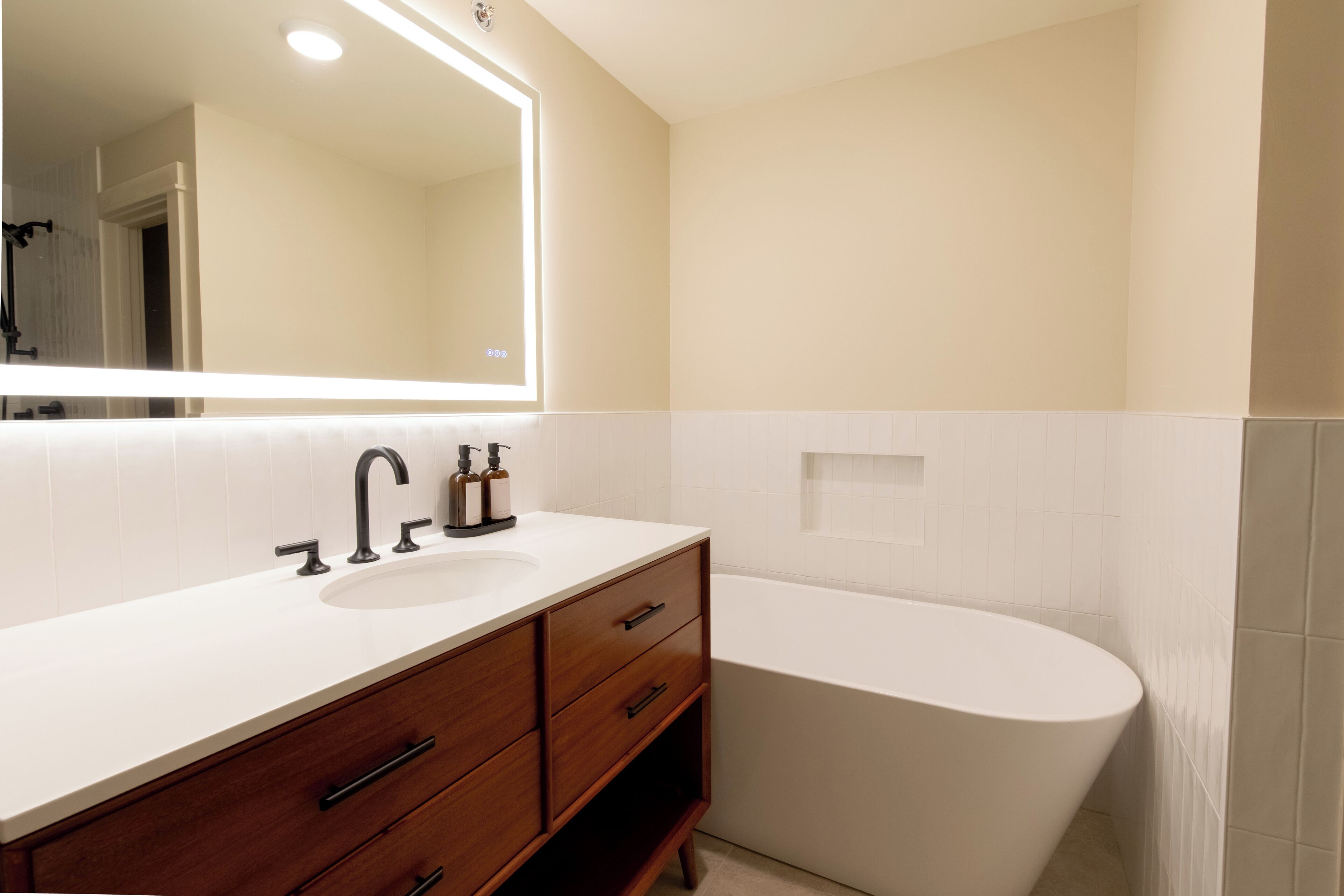 Un baño moderno con lavamanos blanco, tocador de madera y una bañera independiente.