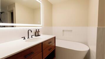A modern bathroom with a white sink, wooden vanity, and a freestanding bathtub.