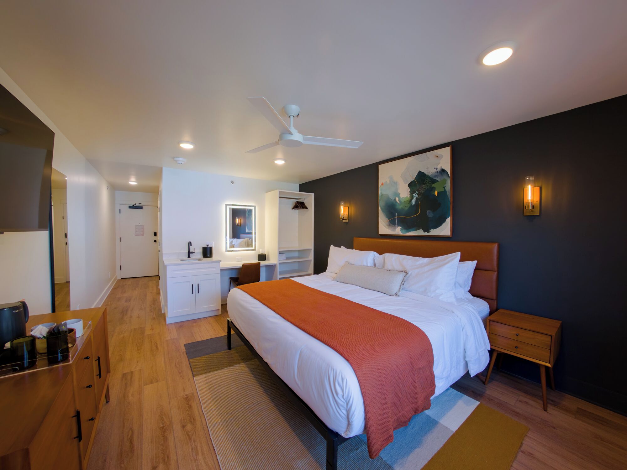 A modern hotel room with a large bed, a desk, a wardrobe, and a ceiling fan.