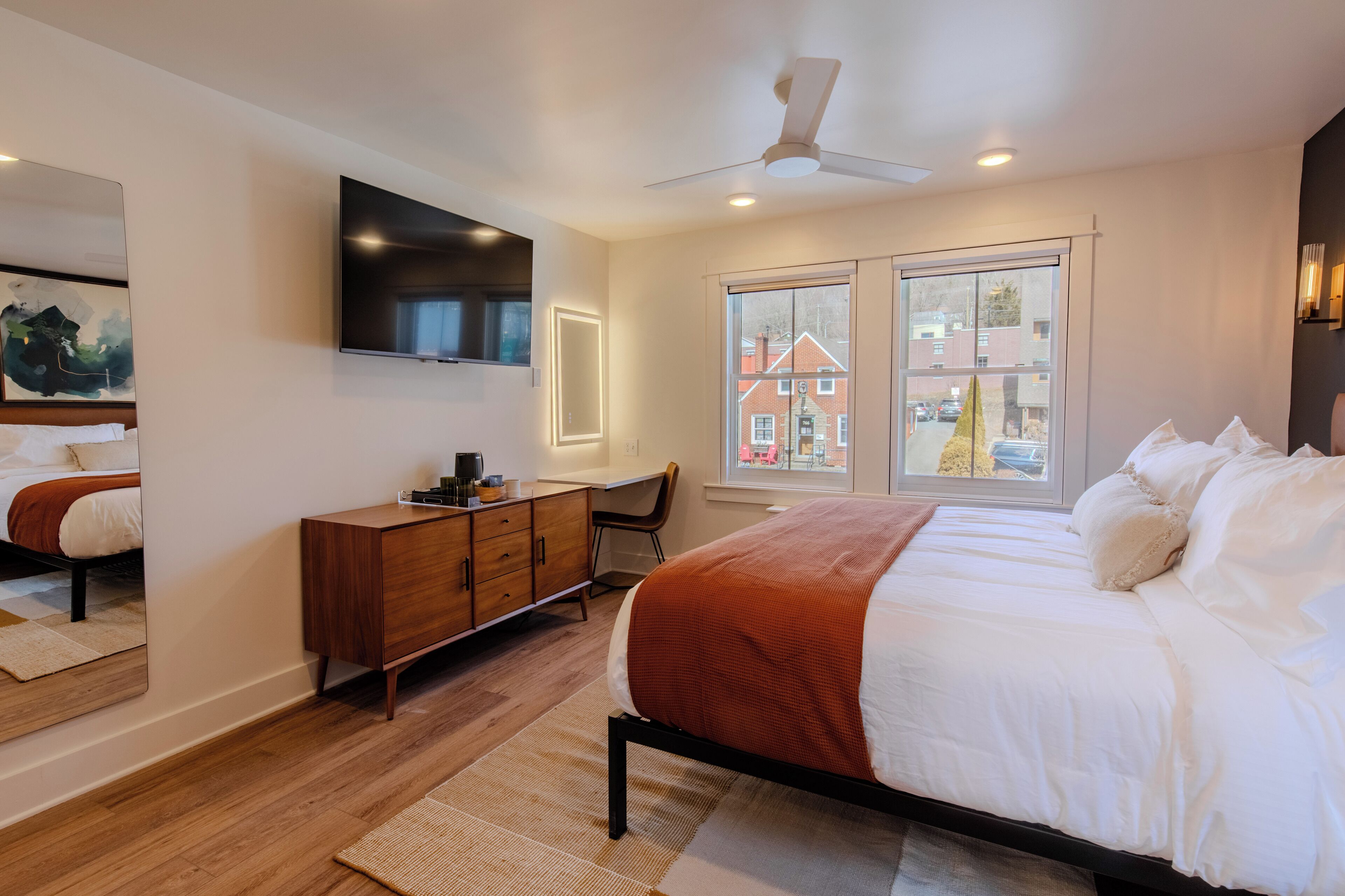 Une chambre à coucher moderne avec un lit, un bureau, un miroir et un téléviseur.