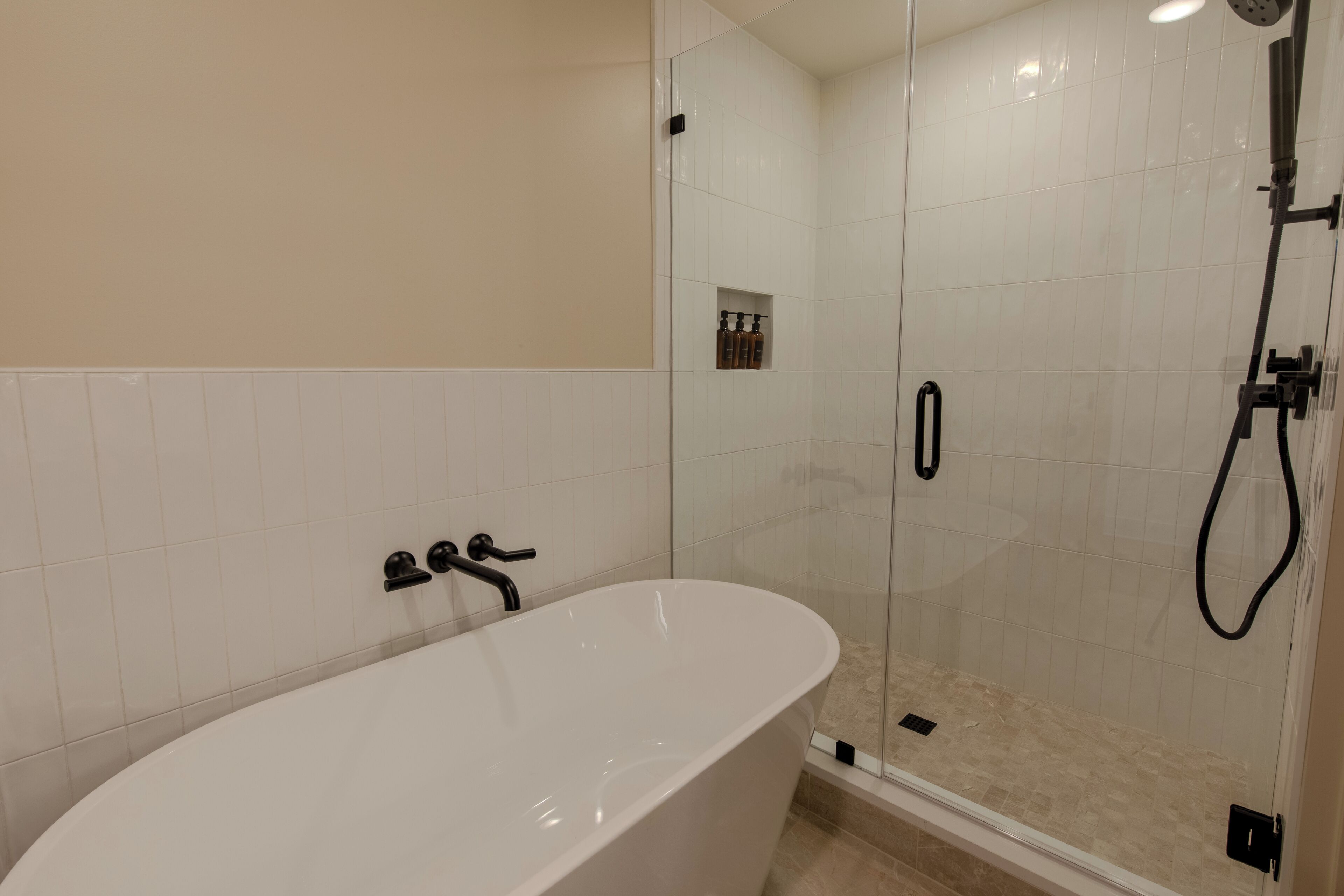 A modern bathroom with a freestanding bathtub, a glass-enclosed shower, and a small shelf with toiletries.