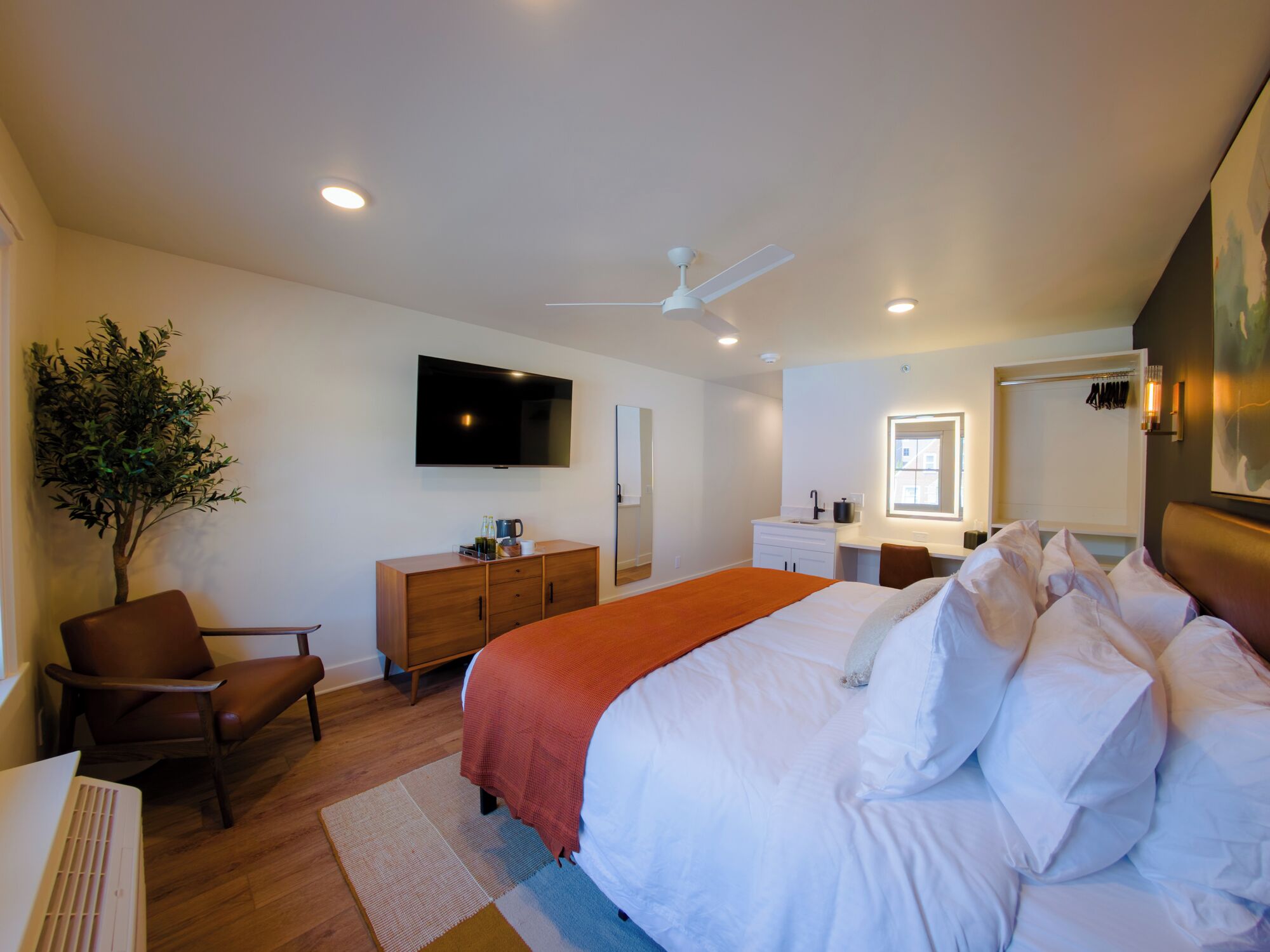 A modern bedroom with a bed, a desk, a chair, a dresser, a television, and a ceiling fan.