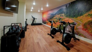 Ein Fitnessstudio mit Trainingsgeräten, Laufband und einer großen Wandmalerei einer schönen Landschaft.
