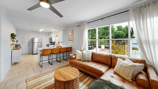 Un salon moderne avec un canapé en cuir marron, une table basse en bois et un coin repas avec une cuisine en arrière-plan.