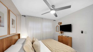 Une chambre à coucher avec un lit, un ventilateur de plafond, une télévision et une commode en bois.