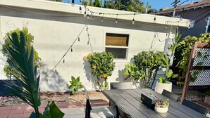 Une terrasse extérieure avec une table et des chaises en bois, entourée de plantes en pot et illuminée par une guirlande lumineuse.
