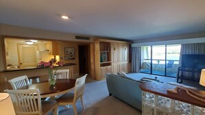 Una sala de estar moderna con un sofá, una mesa de comedor con sillas, una zona de cocina con armarios y un ventanal con vistas al exterior.