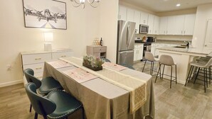 Une cuisine moderne avec des meubles blancs, un réfrigérateur en acier inoxydable et un coin repas avec une table dressée pour quatre personnes.