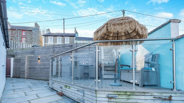 A glass-enclosed outdoor area with a thatched roof, stone flooring, and a view of the surrounding buildings. - 3 bedroom accommodation in New Quay (New Quay)