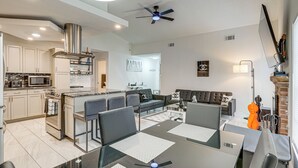 A modern kitchen with a central island, a dining area with a table and chairs, a living room with a sofa, and a fireplace. - 2 Mi to Golfing: Chic & Cozy Retreat in Lakeland! (Lakeland)