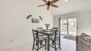 Un'area pranzo con tavolo e sedie, una ventola a soffitto e vista su un patio esterno attraverso una porta in vetro.