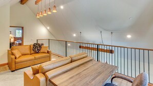 Un loft espacioso con techo alto, una mesa de comedor de madera, sofás de cuero e iluminación colgante.