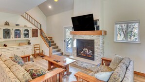 Amplia sala de estar con chimenea, una escalera de madera y un televisor montado en la pared.
