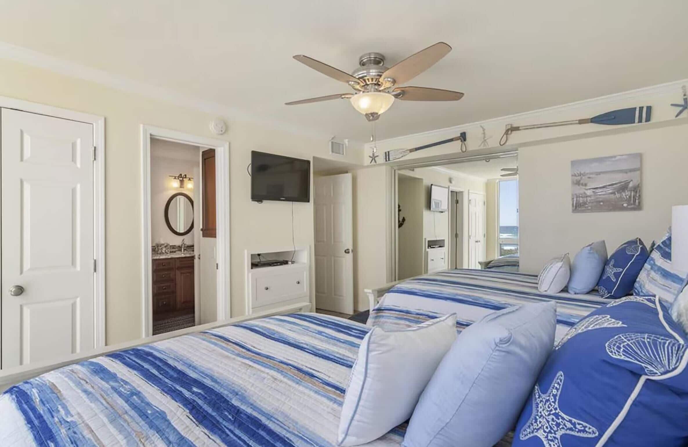 A bedroom with a bed, a ceiling fan, a mirror, and a television.