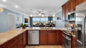 A modern kitchen with granite countertops, wooden cabinets, stainless steel appliances, and a view to the outside. - Shoreline Towers 1022 (Destin)