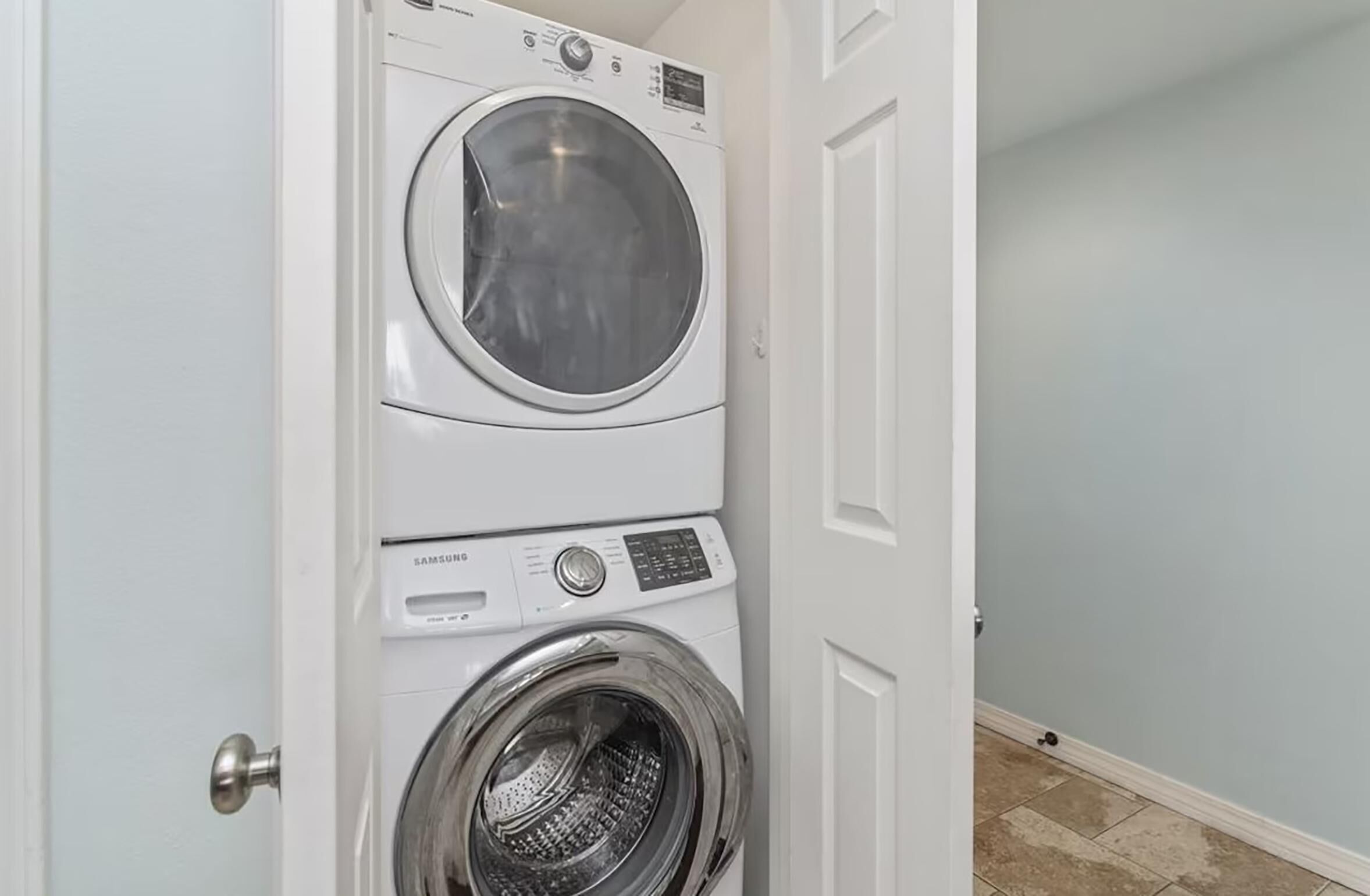 A white wall with a door partially open, revealing a stacked washer and dryer unit.