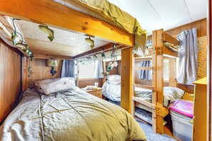 A bunk bed room with a wooden ceiling, a bunk bed on the right, a single bed on the left, and a small table with a lamp. - Hike, Ski & Unwind: Cabin w/ Deck in Chester! (Chester)