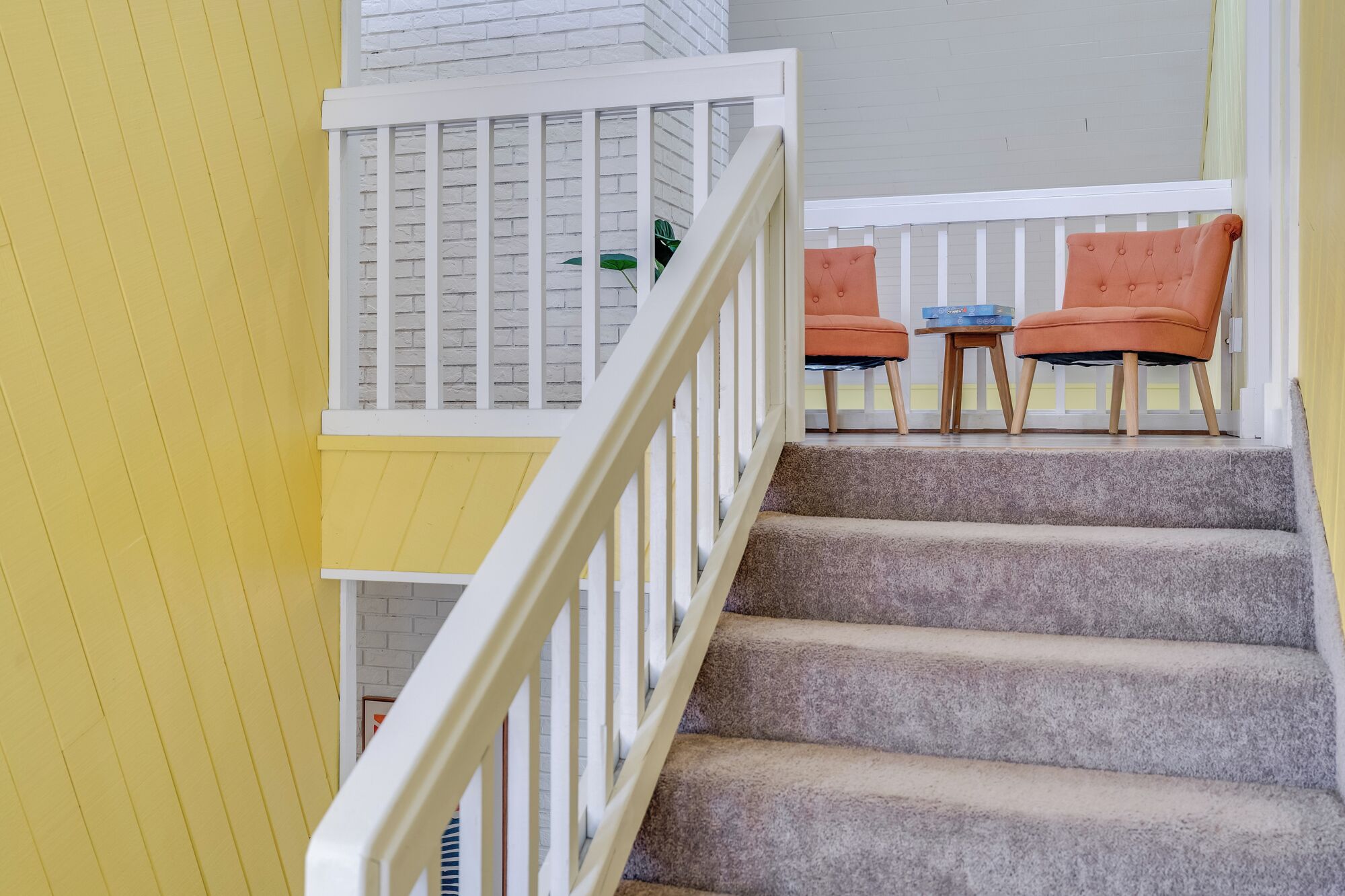 A staircase with a white railing, carpeted steps, and two orange chairs with a small table.