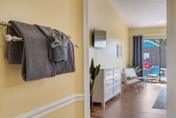 A room with a wooden floor, a white cabinet, a grey towel on a towel rack, and a TV mounted on the wall.