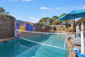 A swimming pool with a colorful mural on the wall, a basketball hoop, and outdoor furniture.