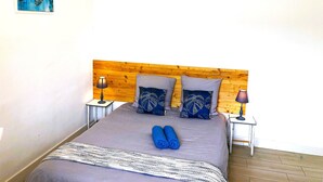 A neatly made bed with a grey bedspread, two pillows with leaf patterns, and two rolled blue towels.