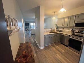 A modern kitchen with stainless steel appliances, a wooden dining table, and a view into the living area. - Charming, 1st floor, 2-bedroom condo in pleasant White Lake with WiFi, AC (Elizabethtown)