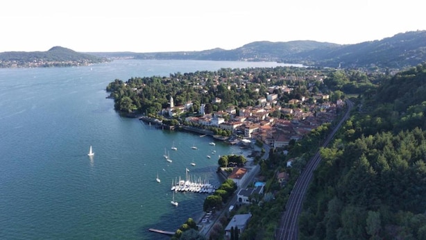 Vista aérea de un pueblo costero con un puerto deportivo, rodeado de colinas y vegetación densa.