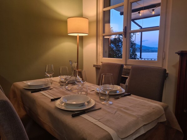 Una mesa de comedor dispuesta con platos, vasos y cubiertos, una lámpara y una ventana con vistas al exterior.