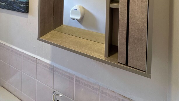 A bathroom with a built-in mirror, a towel dispenser, and a painting of a sailing ship. - Master Suite Platinum #1 (San Pedro Sula)