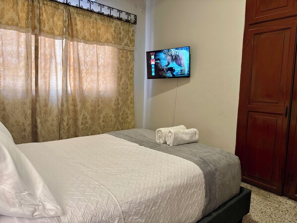 A hotel room with a bed, a TV mounted on the wall, and a wooden wardrobe.