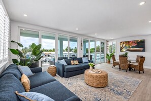 A spacious living area with a dark blue sofa, wicker side tables, and a dining set.