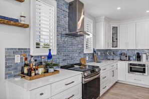 A modern kitchen with white cabinetry, a black stove, and a blue-tiled backsplash.
