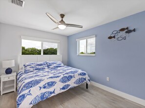 A bedroom with a bed, two windows, a ceiling fan, and a wall decoration.