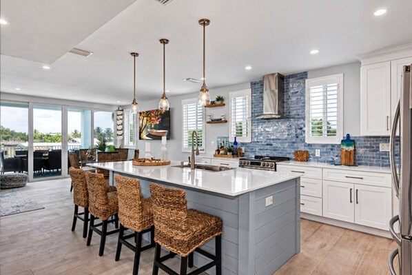 A modern kitchen with a large island, bar stools, pendant lighting, and a view to the outdoors.