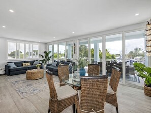 A spacious living area with a large glass door leading to an outdoor balcony, furnished with wicker chairs and a glass table.