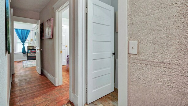 A hallway with wooden flooring, white doors, and a textured wall.