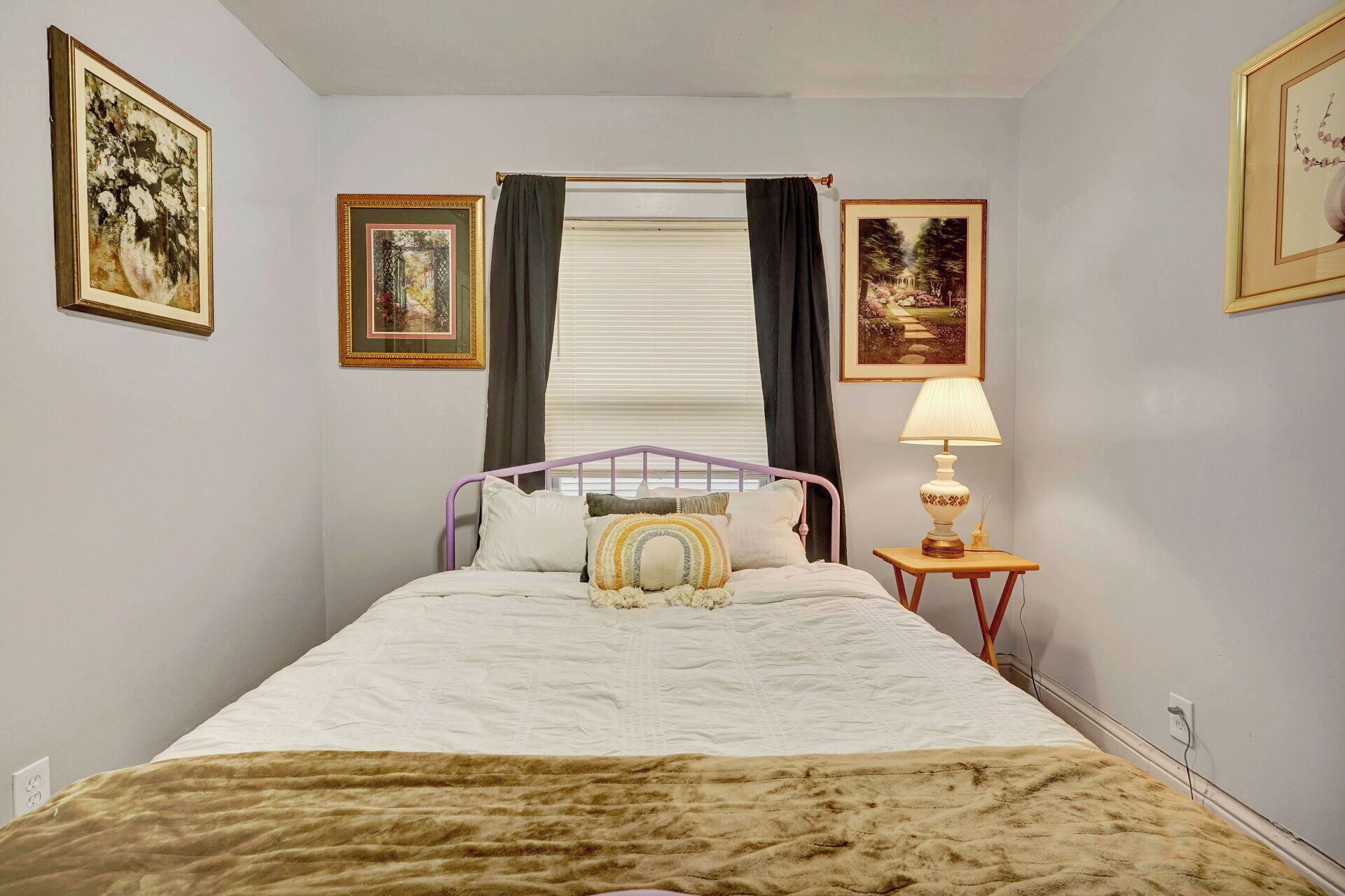 A bedroom with a bed, a bedside table with a lamp, and three framed pictures on the walls.