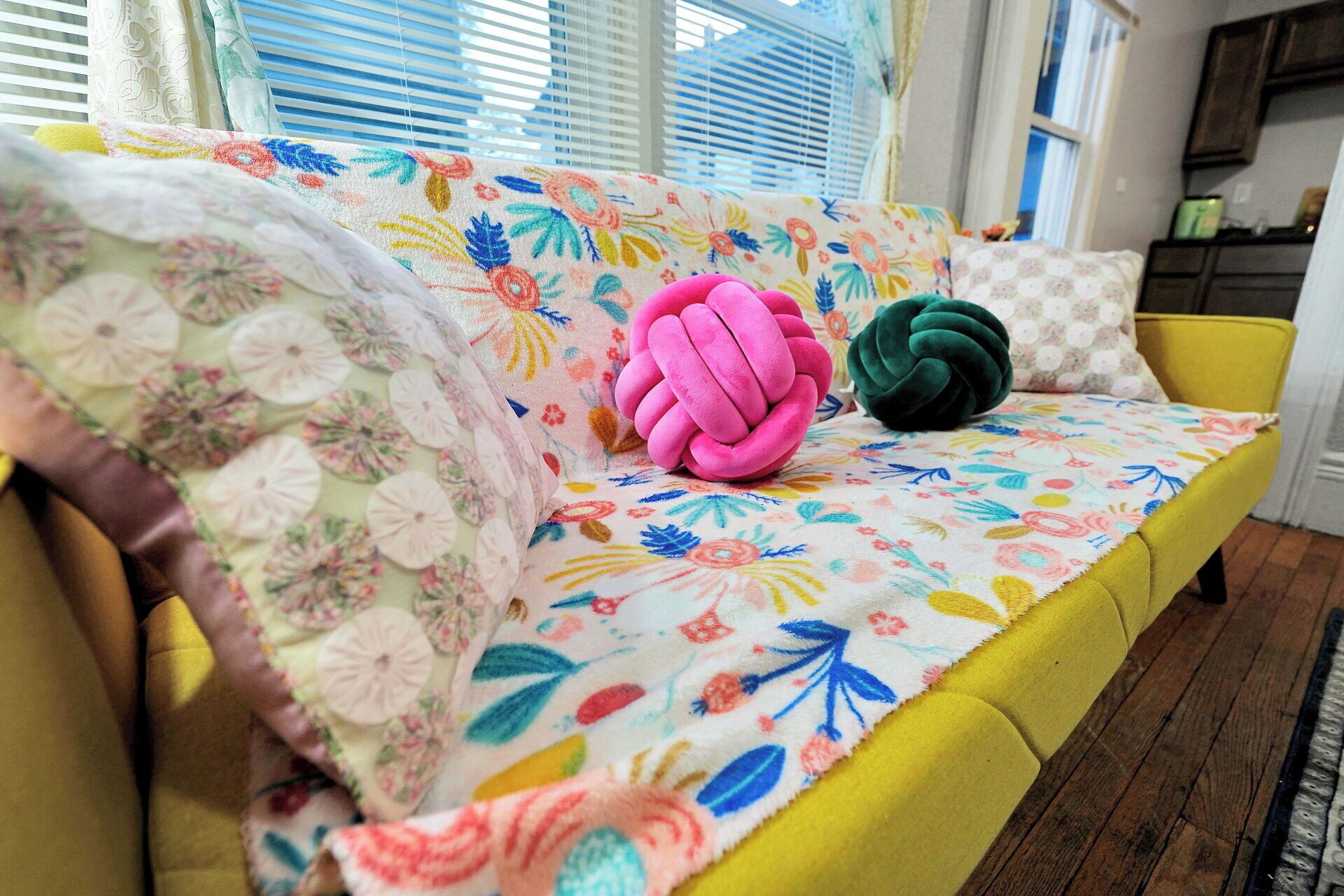 En gul soffa med kuddar i ett blommigt mönster och en färgglad pläd.