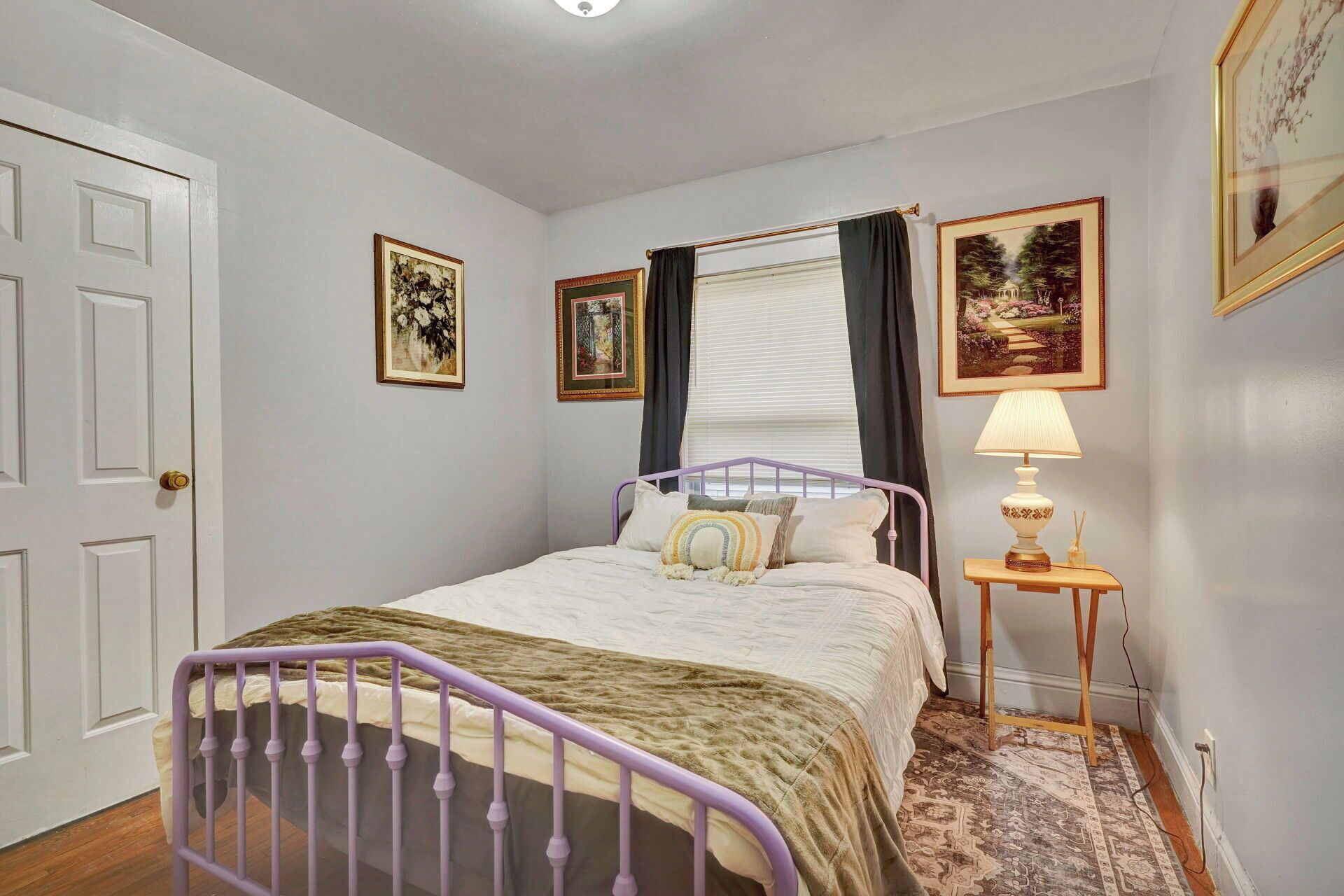 A bedroom with a bed, a nightstand with a lamp, and framed pictures on the wall.