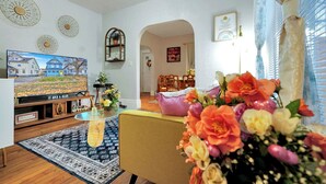 A living room with a television, a coffee table, and a floral arrangement.