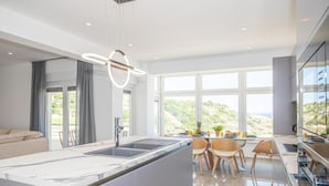 Une cuisine moderne dotée d’un grand îlot central, d’un coin repas avec des chaises et d’une vue sur l’extérieur.
