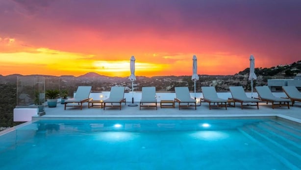 Un espace aménagé au bord de la piscine, avec des chaises longues et des parasols, offrant une vue sur un paysage montagneux au coucher du soleil.